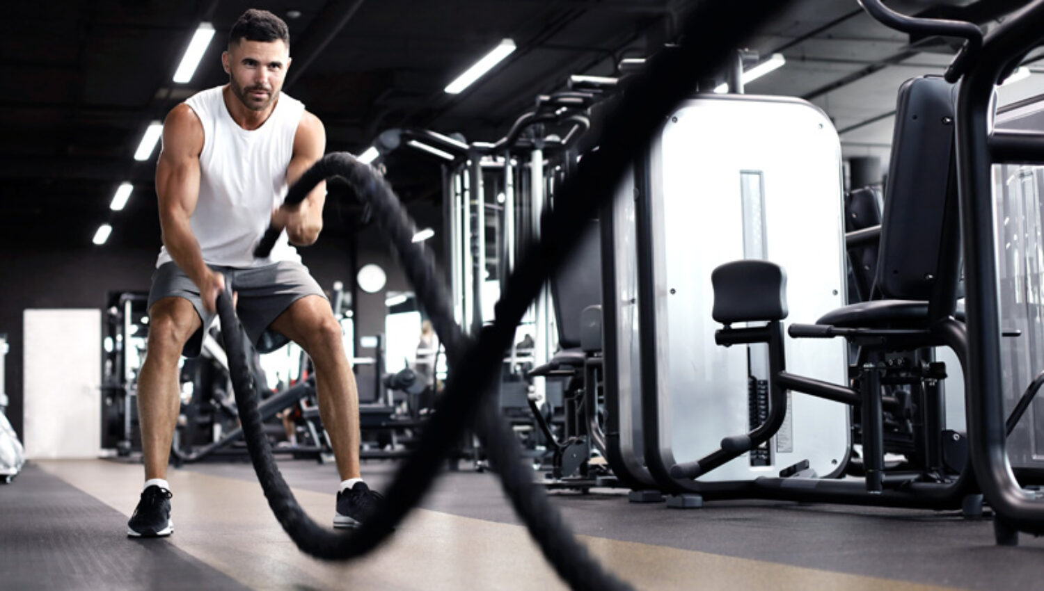 Athletic young man with battle rope doing exercise in functional training fitness gym.