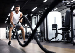 Athletic young man with battle rope doing exercise in functional training fitness gym.