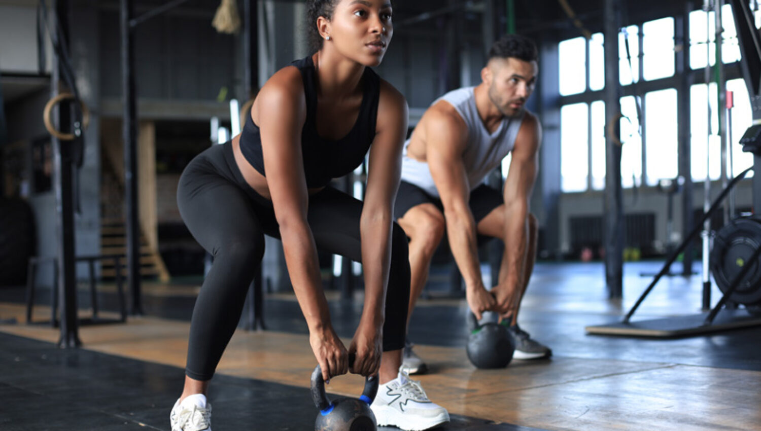 Fit and muscular couple focused on lifting a dumbbell during an exercise class in a gym.