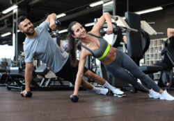 Strong man and woman holding dumbbells in plank position at the gym.