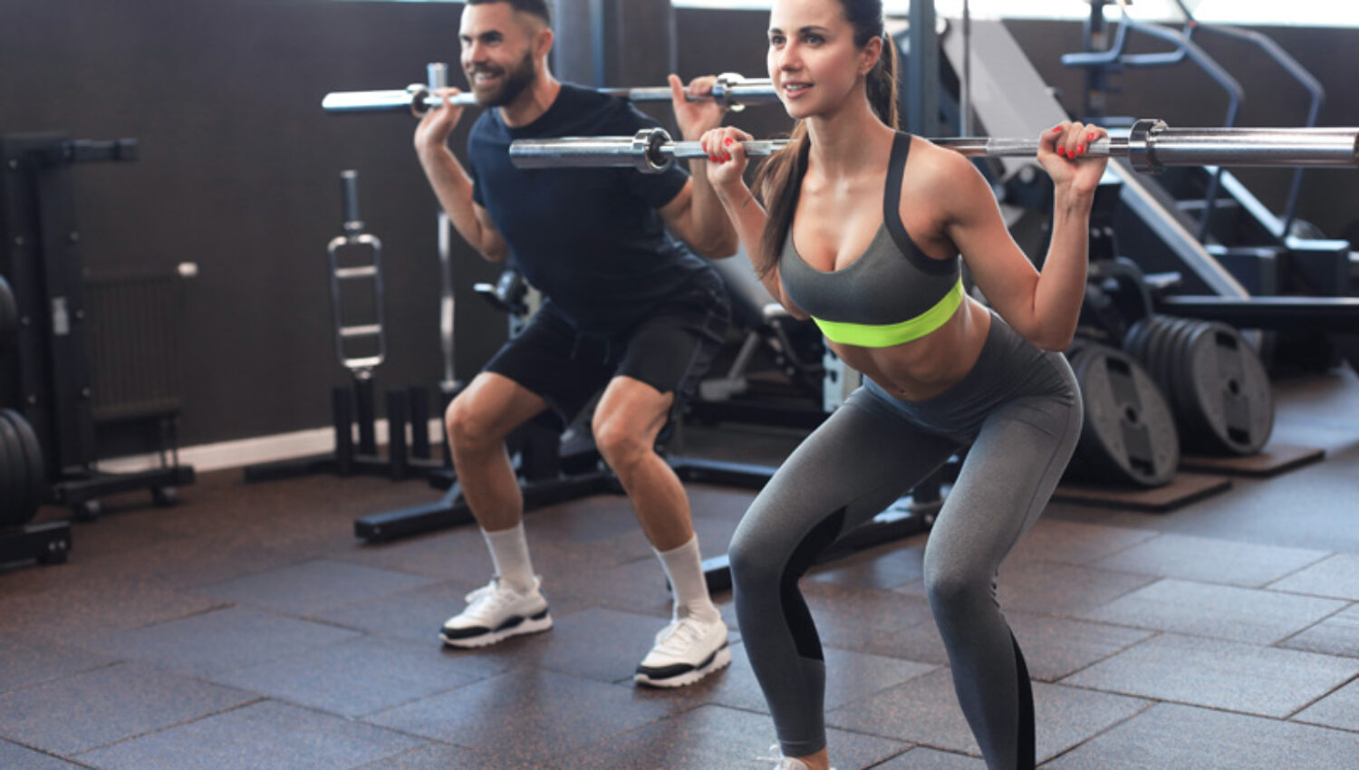 Man and woman with barbell flexing muscles in gym.