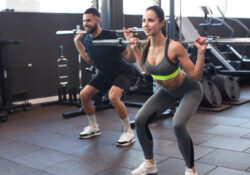 Man and woman with barbell flexing muscles in gym.