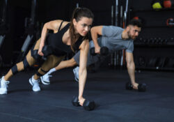 Strong man and woman holding dumbbells in plank position at the gym.
